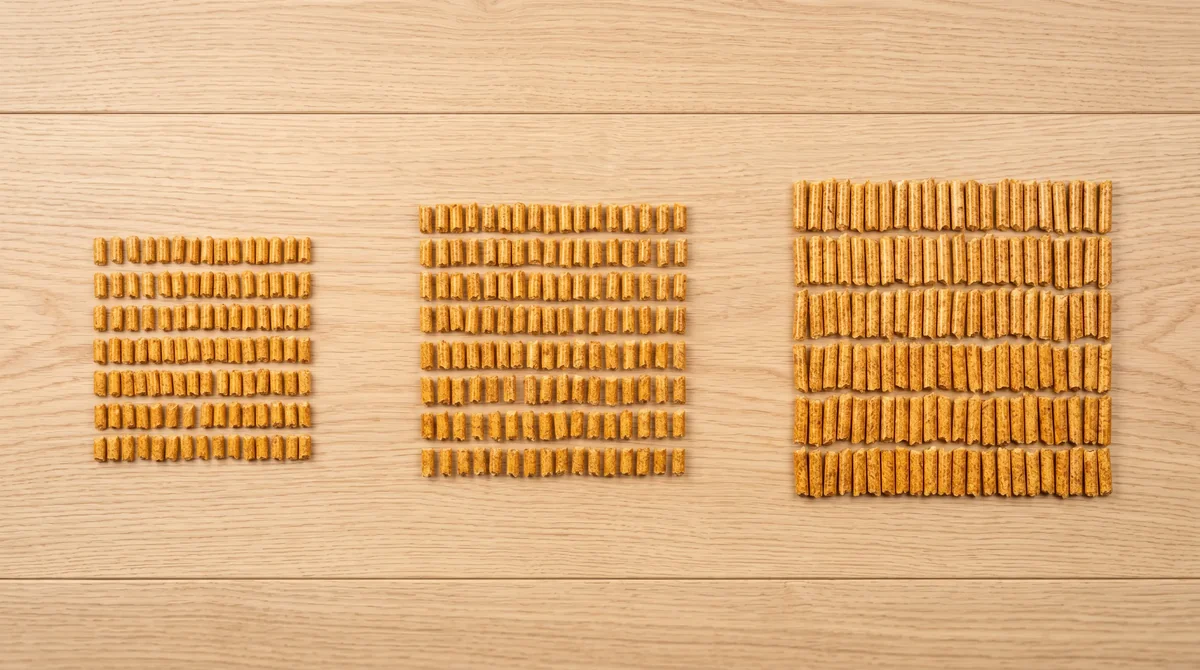 Trzy geometryczne grupy granulatu pelletu drzewnego 6 mm ułożone na jasnych deskach dębowych - norma EN ISO 17225-2 klasy A1 A2 B - ujęcie flat-lay z góry